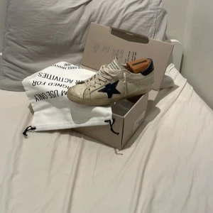 Golden Goose vita sneakers med blå stjärna - Golden Goose sneakers i vitt skinn med ikonisk blå stjärna på sidan och dom är stolk 40 men dom passar som 41 också. Klassisk låg modell . Snygg vintage-look och levereras med originalpåse och låda. Och jag säljer dom på grund av att de är för små för mig nu. Nya  kostar 5000. Kontakta mig om ni är intresserad tack.
