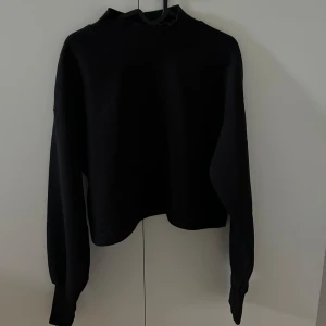 Svart croppad tröja Gina Tricot - Svart croppad tröja från Gina Tricot och har långa ärmar. Tröjan har en loose passform och är tillverkad i mjuk bomullsmix, perfekt för lager-på-lager. Enkel och stilren design som funkar till allt.