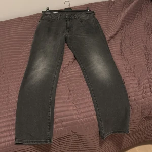 Mörkgråa jeans HM 30/32 - Säljer ett par svarta jeans med raka ben och klassisk femficksdesign. Jeansen har en något tvättad look med ljusare partier på låren och är tillverkade i ett robust jeanstyg. Perfekta för dig som gillar en enkel och stilren vibe. strlk 30/32. Använda 1 gång 