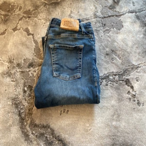 Blå jeans Jack & Jones Regular Clark - Snygga blå jeans från Jack & Jones i modellen Regular Clark. Klassisk femficksdesign med raka ben och normal passform. Jeansen är tillverkade i slitstarkt denimtyg och har en cool tvättad look. Perfekta till vardags med en hoodie eller t-shirt.