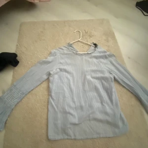 Blåvit randig blus från Vero Moda - Säljer en blåvit randig blus från Vero Moda i storlek M. Blusen har långa ärmar med smockdetalj vid ärmsluten och är tillverkad i ett lätt och luftigt material. Perfekt för dig som gillar en fräsch och stilren look.