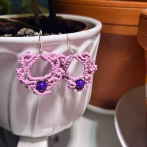 Handgjorda lila örhängen med pärla - Unika handgjorda örhängen i virkad lila tråd med en rund lila pärla i botten. De har en öppen cirkelform och ett lekfullt, bohemiskt uttryck. Perfekta för dig som vill sticka ut med färg och kreativ design.