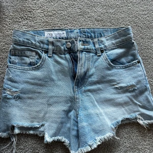 Ljusblå jeansshorts från Zara - Säljer ett par ljusblå jeansshorts från Zara med råa, fransiga kanter och slitna detaljer framtill. Klassisk femficksmodell med knapp och dragkedja. Perfekta för sommarens chill dagar och har en loose passform.