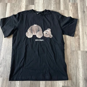 Svart Palm Angels t-shirt med nalletryck - Svart t-shirt från Palm Angels med stort tryck av en sönderdelad nalle på framsidan och Palm Angels-logga i vitt på ryggen. Klassisk rund hals och korta ärmar. Materialet är mjuk bomull som känns skön mot huden. Perfekt för dig som gillar streetwear och coola prints.