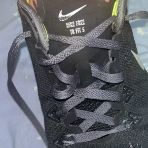 Nike Free TR Fit 5 svarta sneakers - Svarta Nike Free TR Fit 5 sneakers med mesh-ovandel och grå snörning. Snygga detaljer i silver och insida i neongult. Lätta och flexibla skor perfekta för träning eller gym. Klassisk Nike-logga på sidan och plös.