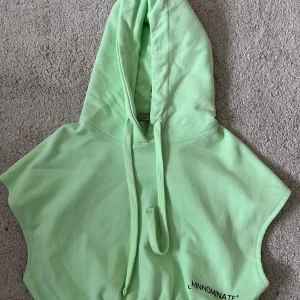 Mintgrön hoodie utan ärmar Hinnominate - Säljer en mintgrön hoodie från Hinnominate med huva och snörning. Tröjan är ärmlös och har en cool, loose passform som passar perfekt till streetwear. Materialet är mjuk bomull och trycket med loggan syns framtill. Perfekt för dig som gillar att sticka ut.