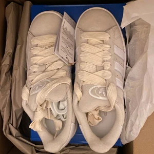 Adidas Campus 00s beiga  sneakers - Fräscha (äkta) Adidas Campus 00s sneakers i ljusbeige mocka med klassiska vita ränder på sidorna. Skorna har rund tå, platt sula och breda snören för en retrovibe. Perfekta för dig som gillar stilrena och tidlösa sneakers med en modern twist. Åkte iväg på semester kom tillbaka och glömde helt bort min retur tid så nu säljer jag de här på Plick istället. Nypris 1 449 kr