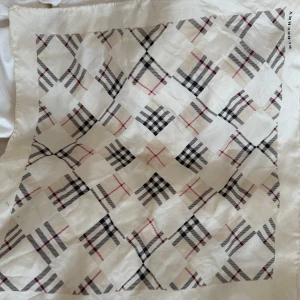 Burberry rutig sidenscarf - Snygg och klassisk halsduk från Burberry i siden med det ikoniska rutiga mönstret i svart, rött och beige på vit botten. Perfekt storlek för att ha runt halsen eller som accessoar. Diskret Burberry-logga i hörnet.