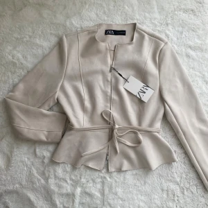 Suede jacka från Zara - Helt ny oanvänd suede jacka från Zara. dragkedja upptill och nertill. bälte går att ta bort (snöre). beige/vit 