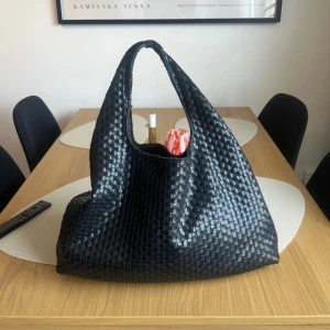 Svart handväska i flätad skinnlook NA-KD - Säljer en svart handväska från NA-KD med snygg flätad design i skinnimitation. Väskan har en mjuk, rymlig form och ett handtag som gör den enkel att bära. Perfekt för dig som vill ha en trendig och stilren accessoar till vardagen.