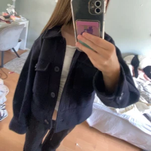 Marinblå overshirt med stora knappar - Säljer en marinblå overshirt med oversized passform och stora knappar framtill. Jackan har en klassisk krage, bröstficka med lock och långa ärmar. Perfekt för hösten.