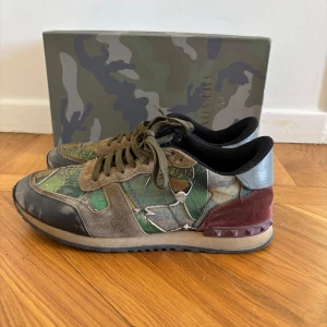 Valentino Rockrunner sneakers camouflage - Snygga Valentino Rockrunner sneakers med camouflage-mönster i grönt, brunt och svart. Skorna har detaljer i mocka, skinn och textil samt ikoniska nitar på hälen. Perfekta för dig som vill sticka ut med en cool streetstyle-look. Box ingår inte