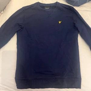 Mörkblå sweatshirt från Lyle & Scott - Mörkblå sweatshirt från Lyle & Scott med klassisk rund hals och gul logga broderad på bröstet. Tröjan har långa ärmar, ribbade muddar och är tillverkad i mjuk bomull. Storlek M. Köpt för 999kr. Säljer för 350kr. Pris kan diskuteras, stick 9/10. Vid frågor eller intresse skriv!