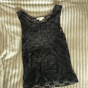 Svart spetsig linnetopp från Gina Tricot - Säljer en svart linnetopp från Gina Tricot i genombruten spets med blommigt mönster. Toppen har rund halsringning och är perfekt för att skapa en cool lager-på-lager-look. Superfin detalj med spetsen längs kanterna.