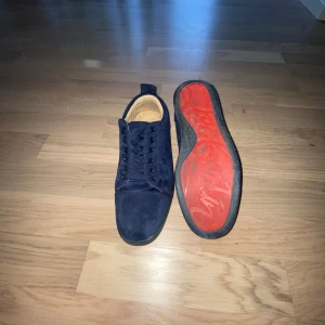 Mörkblåa Christian Louboutin  - Snygga mörkblå sneakers i mocka från Christian Louboutin med rund tå och platt sula. Skorna har matchande blå snörning och diskret broderad logga bak på hälen. Perfekta för dig som gillar stilrena och exklusiva sneakers.