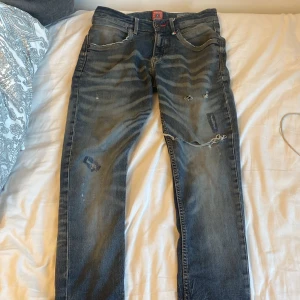 Blå slitna jeans från Vingino - Säljer ett par blå jeans från Vingino med coola slitningar och lagade detaljer. Jeansen har regular fit, klassisk femficksdesign och snygga kontrastsömmar. Perfekta för dig som gillar en avslappnad och trendig look.