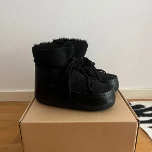 Svarta Inuikii moon boots i mocka - Säljer ett par svarta Inuikii moon boots med snörning och mjukt foder. Skorna är i mocka och har en rejäl platt sula, perfekt för kalla dagar. Klassisk rund tå och snyggt detaljerade med grova snören som går kors och tvärs över skon. Endast använda en månad, nypris 3799kr