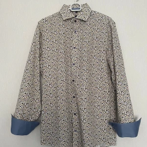 Mönstrad skjorta från Venti, strl 40 - Snygg skjorta från Venti med coolt djur- och naturmönster i blått, brunt och grönt på vit botten. Modern fit med långa ärmar och kontrastfärgade blå manschetter. Perfekt för dig som vill sticka ut lite extra med din stil.