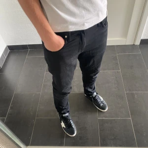 Svarta jeansbyxor från Tiger of Sweden - Säljer ett par svarta jeansbyxor från Tiger of Sweden, modell Pistolero. Byxorna har en slim passform och klassisk femficksdesign. Snyggt läderpatch bak i midjan och diskreta detaljer. Perfekta för dig som gillar stilrena och moderna jeans.