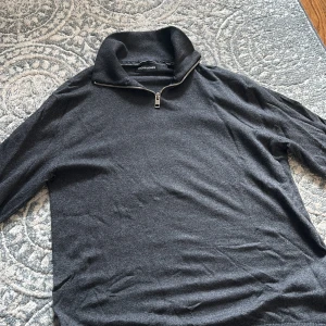 Mörkgrå half zip tröja Jack & Jones  - Mörkgrå långärmad tröja från Jack & Jones med hög krage och half zip-dragkedja. Tröjan är i mjukt material och har en clean, stilren look som passar perfekt till lager-på-lager. Enkel att matcha med jeans eller chinos.