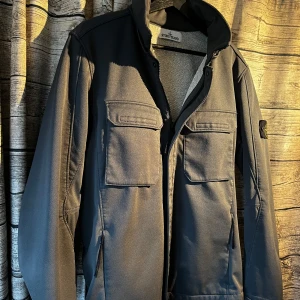 Grön jacka från Stone Island - Säljer en fräsch och stilren Stone Island jacka i storlek L. Modellen är Soft Shell-R Terry Färg: Mörkgrön Storlek: L Material: 3-lagers softshell med vatten- och vindresistenta egenskaper Detaljer: Avtagbar patch på ärmen, flera praktiska fickor framtill, hög krage, infällbar luva Skick: Mycket bra, sparsamt använd Jackan är både vattenresistent, vindtät och andas – perfekt för höst, vår och milda vinterdagar. Kan gå ned i pris vid snabb och smidig affär 