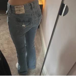 True Religion bootcut jeans ljusblå - Säljer ett par ikoniska ljusblå bootcut jeans från True Religion med klassiska detaljer på bakfickorna och silverfärgad knapp. Lågmidjade och i mjukt denimtyg, perfekta för dig som gillar en avslappnad men ändå snygg look. Dem har små hål i skrevet men det syns inte och hålen är igen sydda.