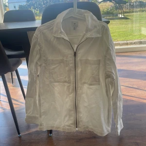 Vit overshirt från H&M med dragkedja - Säljer en stilren vit overshirt från H&M med två stora bröstfickor och dragkedja framtill. 