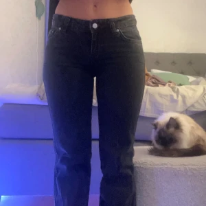 Svarta bootcut jeans med fickdetaljer - Säljer ett par svarta jeans med bootcut-modell och snygga fickor med lock och knapp bak. Jeansen har hög midja och klassisk femficksdesign. Perfekta för dig som gillar en tidlös look med lite extra edge.