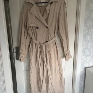 H&M trenchcoat - H&M trenchcoat som aldrig är använd men behöver strykas. Den är super fin och är i storlek S men passar S-XL den har många fina detaljer och är aldrig använd. Behöver endast strykas 