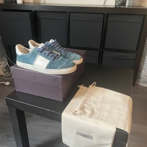 Valentino Garavani blå sneakers - Snygga blå sneakers från Valentino Garavani med vita detaljer och matchande blå snören. Skorna har en rund tå och platt sula med coolt kamouflagemönster undertill. Ovandelen är i mocka och skinn, och medföljer original dustbag och låda. Perfekt för dig som gillar exklusiva märken.
