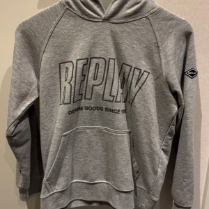 Replay Hoodie - Snygg grå hoodie från Replay med stort tryck på bröstet och logga på ärmen. Klassisk känguruficka framtill och huva. Använd max 3 gånger, mycket fint skick/ny skick!