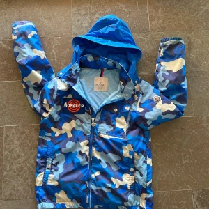 Moncler windbreaker - Säljer en blå camo vindjacka från Moncler med huva och dragkedja.köpte den i Alperna för något årsedan nypris 6700.Den är perkeft nu till hösten och väldigt bra skick.Den passar 164 men passar mig som är 170.Den är självklart äkta.Pris kan diskuteras.