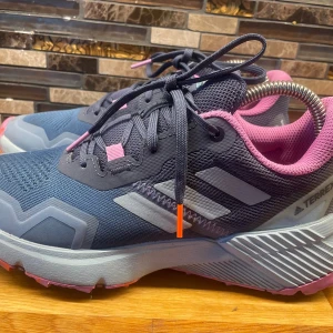 Adidas Terrex sneakers blå/rosa 37⅓ - Snygga Adidas Terrex sneakers i mörkblått med rosa detaljer och grå sula. Ovandelen är i mesh och syntet, med klassiska tre ränder på sidan och extra vadderad rosa insida. Perfekta för dig som gillar sportig stil och outdoor-vibe.