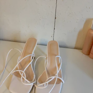 Vita sandaler med snörning och klack - Trendiga vita sandaler med fyrkantig tå, tunna remmar som snöras runt foten och hög klack. Snygg minimalistisk design som ger en clean look. Perfekta för dig som gillar stilrena och moderna skor.