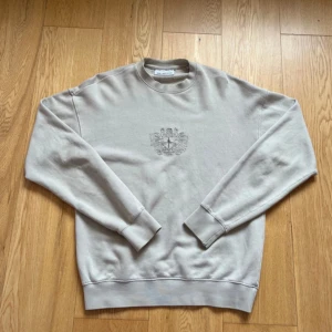 Beige sweatshirt från Han Kjøbenhavn - Snygg beige sweatshirt från Han Kjøbenhavn med broderad logga och emblem på bröstet. Tröjan är i St S och mycket bra skick. Finns bara en defekt som är den svarta pricken (se bild), annars är den fel fri. Ny pris 1620 kr.