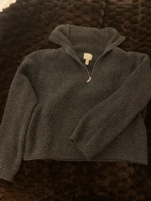 Mörkgrå stickad half zip från H&M - Mysig mörkgrå stickad tröja från H&M med half zip-dragkedja och hög krage. Perfekt för kyliga dagar och enkel att styla med jeans eller kjol. Tröjan har långärmad passform och ribbad struktur för extra komfort. Köpt för 400kr.