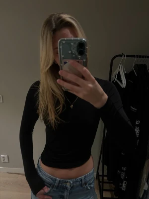 Svart långärmad topp med öppen rygg Nelly - Svart långärmad topp från Nelly med croppad passform och öppen rygg som knyts med band. Tillverkad i stretchigt material som sitter snyggt på kroppen. Perfekt för dig som vill ha en stilren men ändå unik look.