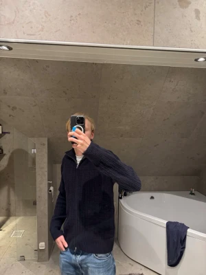 Mörkblå stickad zip tröja - Säljer en mörkblå stickad tröja med zip och hög krage. Tröjan har ett snyggt ribbat mönster och är långärmad, perfekt för kyligare dagar. Passar dig som gillar en enkel men stilren look. Storlek s men sitter mer som m