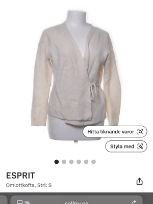 Beige omlottkofta från Esprit - Mysig beige omlottkofta från Esprit i mjuk stickad kvalitet. Koftan har långa ärmar och knyts i sidan för en avslappnad look. Perfekt att slänga på sig över en topp när det är lite kyligt ute.