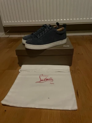 Mörkblå mocka sneakers Christian Louboutin - Snygga mörkblå sneakers från Christian Louboutin i mjuk mocka med klassisk röd sula och vita kanter. Skorna har rund tå, snörning och en stilren design som passar till det mesta. Kommer med original dustbag och låda.