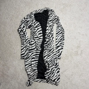Zebramönstrad kofta från Object XS - Säljer en lång, öppen kofta från Object i storlek XS med svartvitt zebramönster. Koftan har lång ärm och är gjord i ett mjukt, tunt material som känns skönt mot huden. Perfekt för dig som vill sticka ut med ett djurmönster i garderoben.