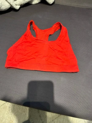 Röd sportväst från Casall - Säljer en röd sportväst från Casall med brottarrygg och meshdetaljer för extra ventilation. Västen är tillverkad i ett stretchigt syntetmaterial som passar perfekt till träning. Enkel och stilren design utan mönster.