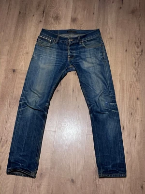 Nudie Jeans Grim Tim Dry Selvage - Säljer tyvärr mina riktigt feta Nudie Selvage, jeansen är i fint skick med riktigt schyssta honeycombs, whiskers, slitningar och sahsico stygn. De är lagade i skrevet och lite andra ställen men är i fint skick. De är i storlek 32/32 och sitter perfekt på mig 180cm 70kg. Vid några som helst frågor så är det bara att skriva. Nypris 2500
