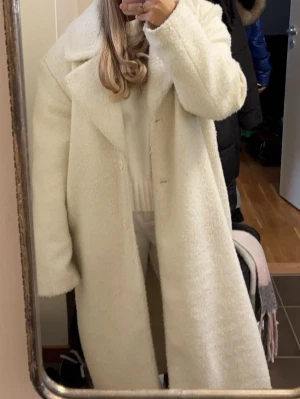 Vit teddyjacka med oversized passform - Säljer en fluffig och lång vit teddyjacka med stora slag och knappar framtill. Jackan har en oversized look och är perfekt för kalla dagar. Den är helvit och har långa ärmar för extra mysfaktor.