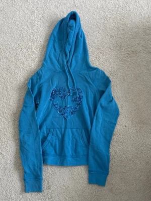 Blå hoodie från Hollister i strl S - Hoodie från Hollister med glittrig detalj på framsidan. Väldigt mysig och skön, snygg färgklick i garderoben