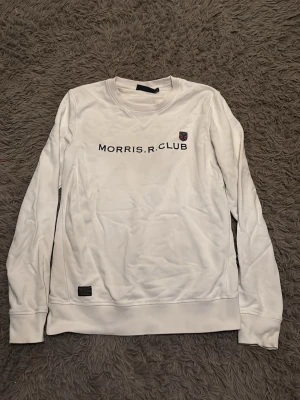 Vit sweatshirt från Morris R Club - Vit sweatshirt från Morris R Club med broderad logga och text på bröstet. Klassisk rund halsringning och långa ärmar. Tillverkad i mjuk bomull för skön känsla. Perfekt till jeans eller chinos för en clean look. Använd mycket men har några år kvar på sig. Finns ett litet hål på höger arm men det är inget synligt🤗kom dm om du har frågor om tröjan✌️