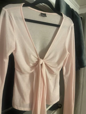 Ljusrosa omlottopp med knyt - Supersöt ljusrosa omlottopp från Shein med lång ärm och djup v-ringning. Toppen har en snygg knytning framtill som ger en feminin touch. Tillverkad i mjukt och stretchigt material som känns skönt mot huden. Perfekt att styla med jeans eller kjol.