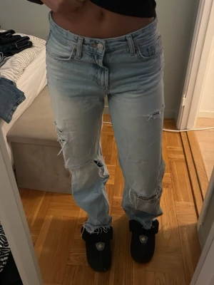 Ljusa ripped jeans från Zara - Säljer ett par ljusblå jeans från Zara med snygga slitningar och hål på både fram- och baksida. Modellen är rak med normal passform