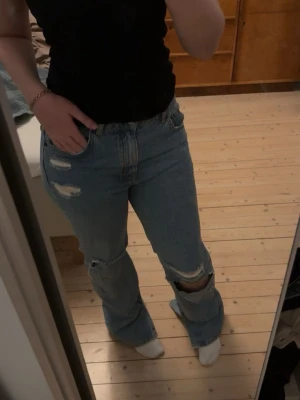 Blå slitna bootcut jeans - Ett par ljusblå jeans med slitningar och hål på knäna. Byxorna har en bootcut passform och  femficksdesign. Har bara använt 2-3 gånger. 