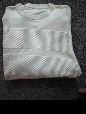 Vit stickad tröja från Selected Homme storlek XXL - Säljer en vit stickad tröja från Selected Homme. Tröjan har ett strukturerat mönster med breda partier av små bollar över bröst, ärmar och nederkant. Rund halsringning och långa ärmar med ribbade muddar. Perfekt för dig som gillar stilrena och moderna plagg.